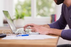 Close up low angle view of a man working from home on a laptop computer sitting at a desk surfing the internet-1