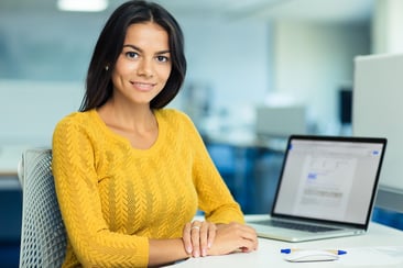 Portrait of a happy casual businesswoman in sweater sitting at her workplace in office